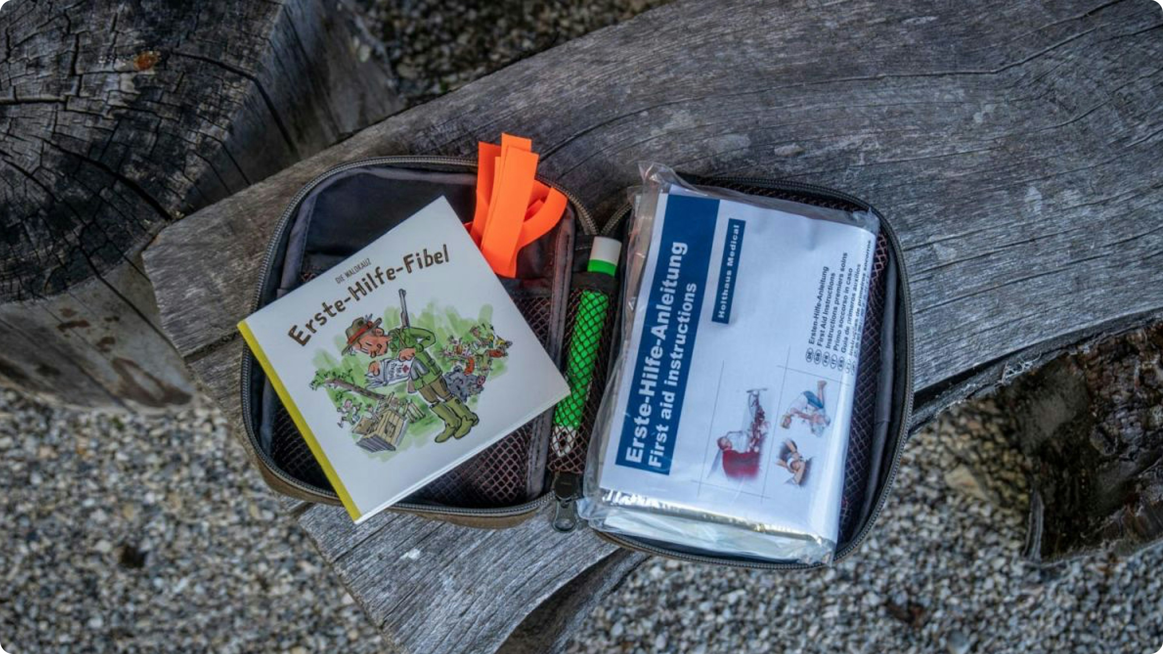 Offenes Erste-Hilfe-Set mit Anleitung und Zubehör auf Holzbank im Freien