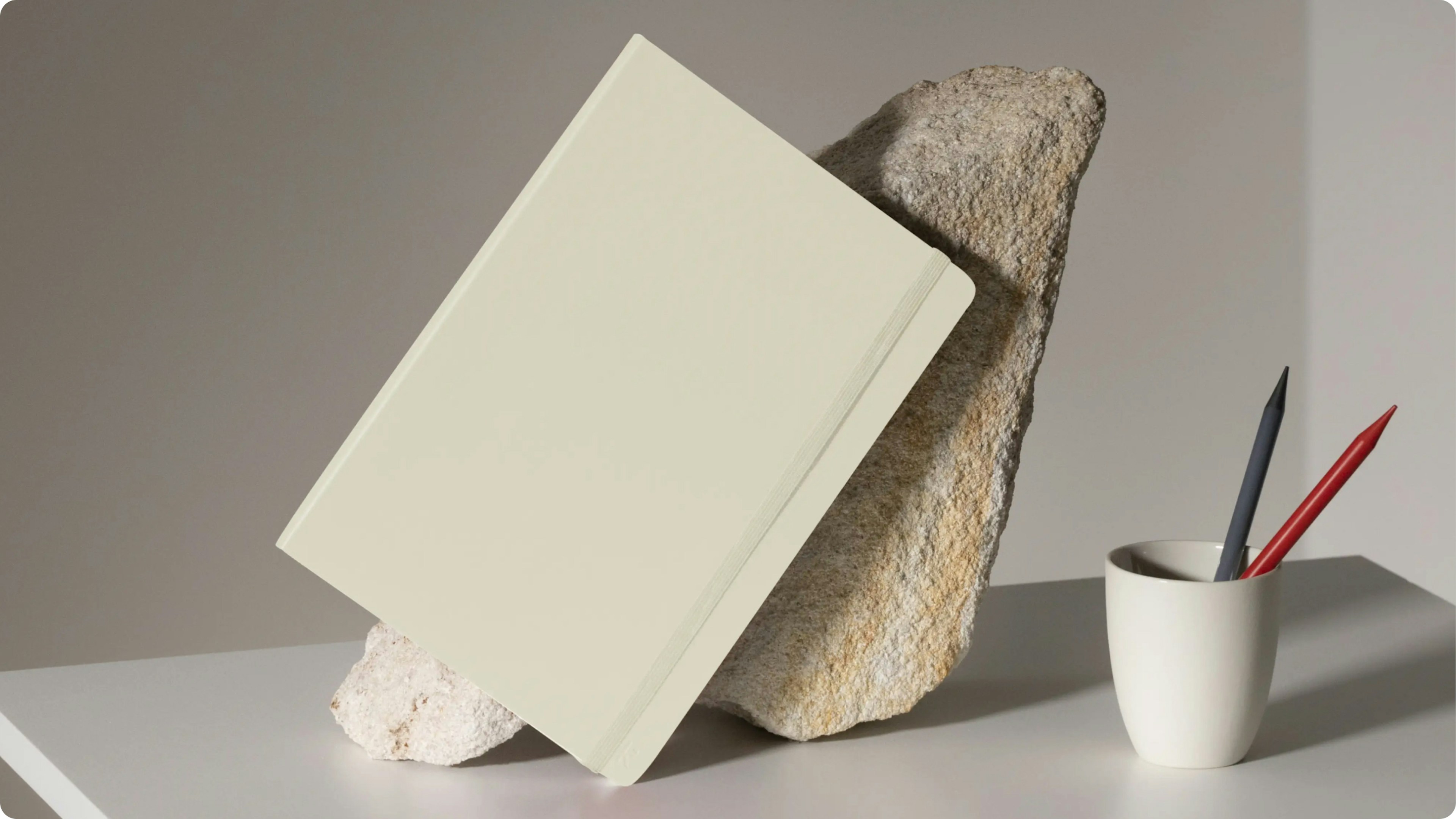 Minimal notebook propped on stone beside a cup holding pens